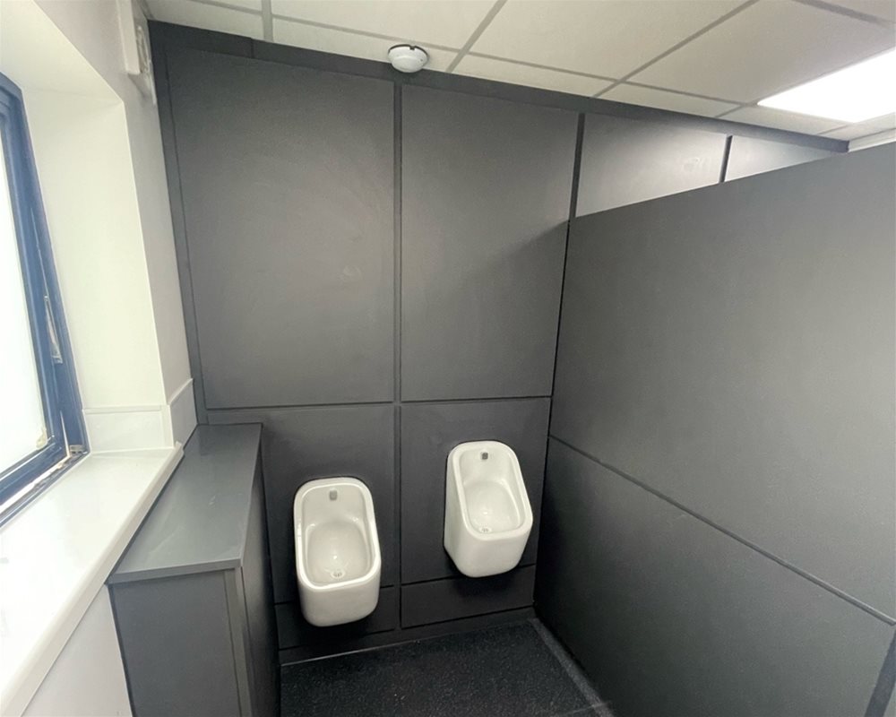 Dark grey duct panels and flashgaps with white ceramic urinals hung at two heights to accommodate users.