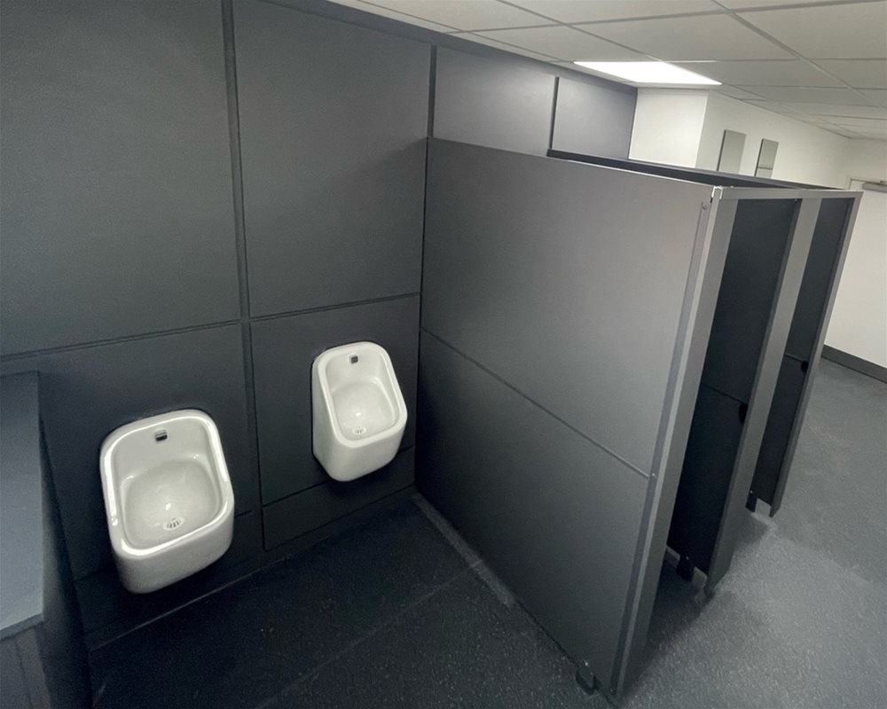 Dark grey duct panels and flashgaps with white ceramic urinals hung at two heights to accommodate users. Dark Grey standard height modular toilet cubicles.